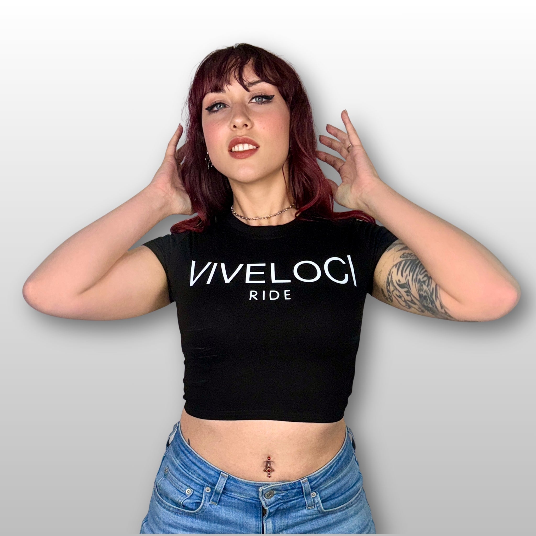 Megan is wearing a black ViVeloci RIDE short sleeved crop top and blue jeans against a gray background