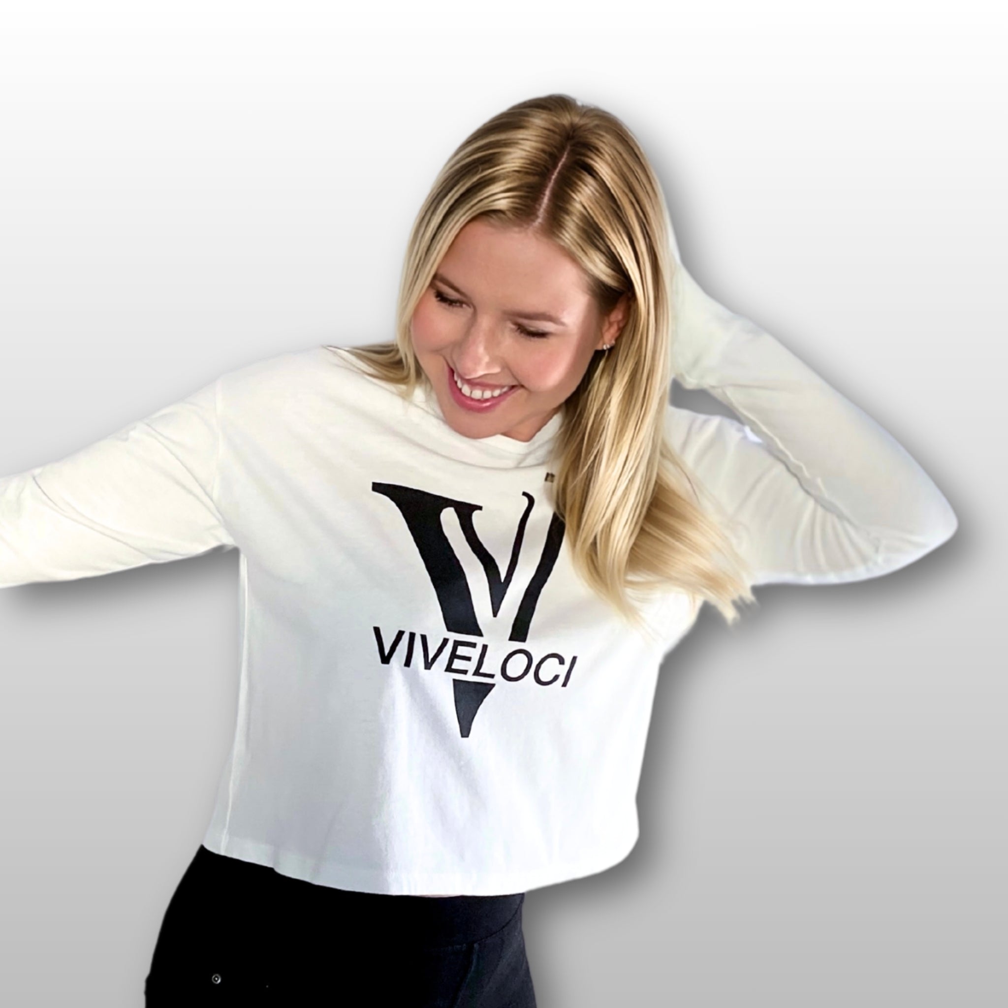 Magdalena wearing a white ViVeloci long sleeved crop top against a grey background.