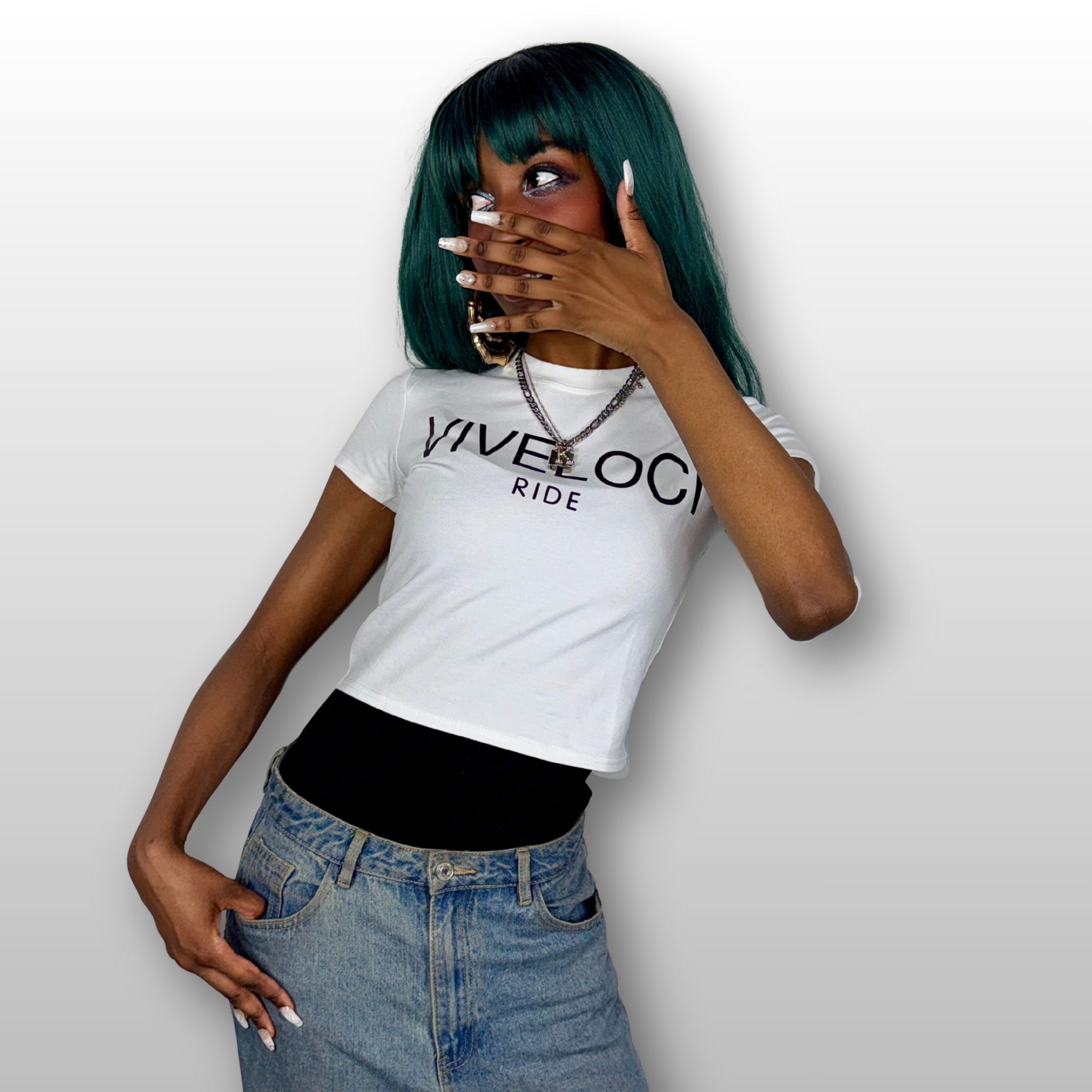 Camaria is wearing a white ViVeloci RIDE short sleeved crop top and blue jeans against a gray background