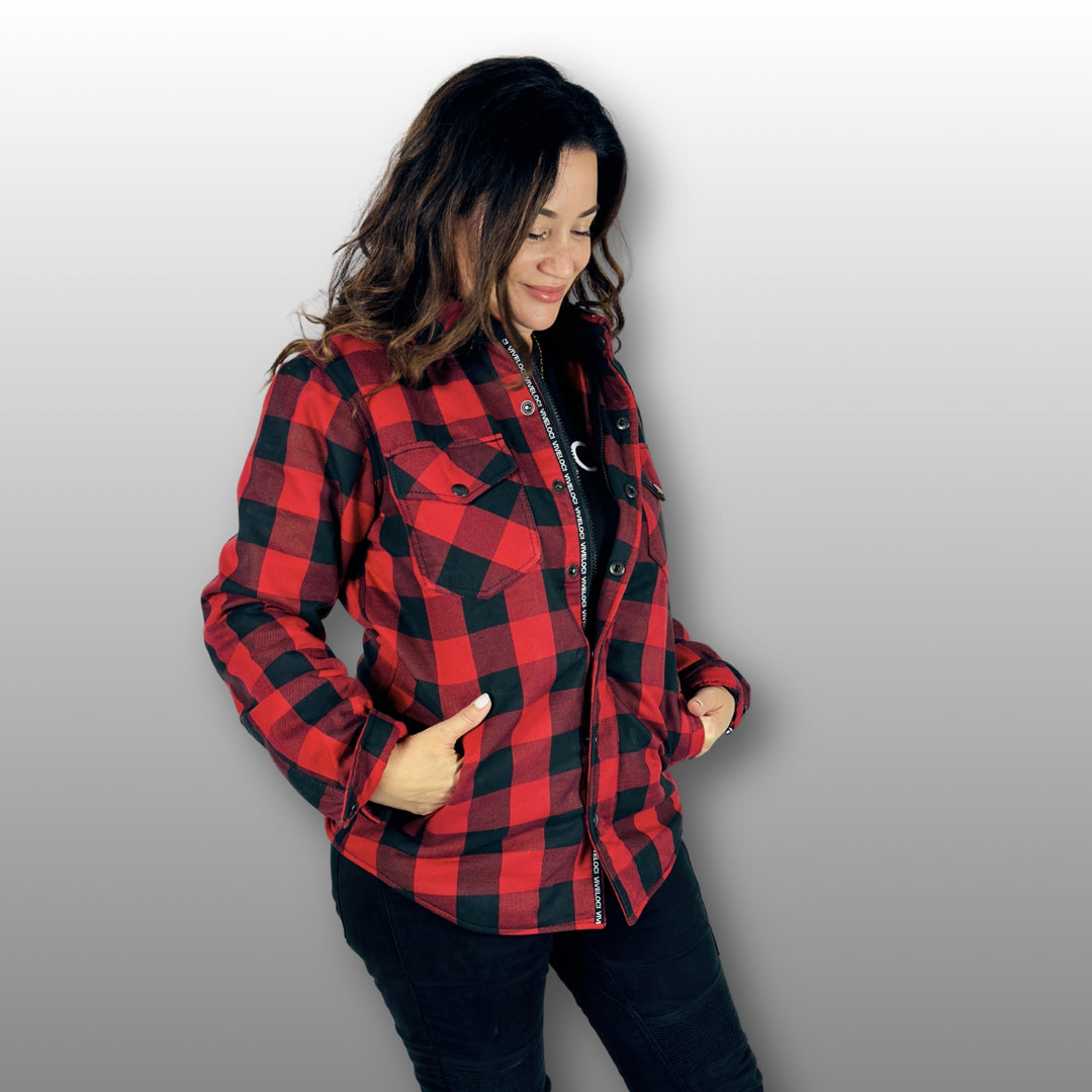 A woman wearing a red and black riding flannel button-up shirt over a black bodysuit, posing against a light gray gradient background.