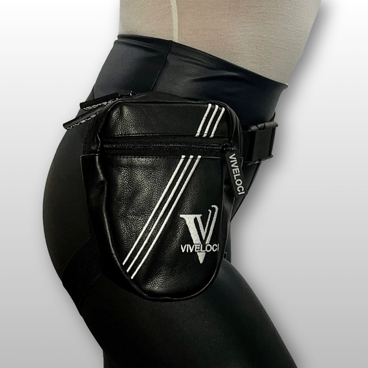 A black leather thigh bag with white diagonal stripes and a white 'VIVELOC1' logo, worn on a model's hip.