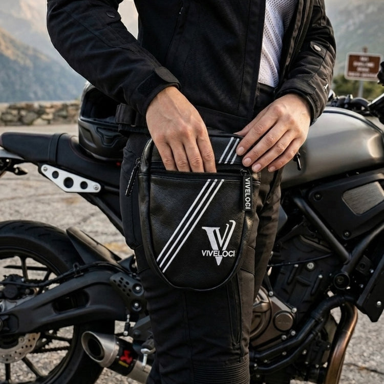 A close-up of a person wearing black motorcycle pants and a black jacket, holding a black ViVeloci Thigh Bag with white stripes and logo, standing next to a motorcycle outdoors.